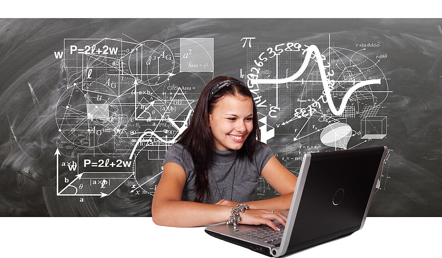 Smiling girl studying math on laptop with chalkboard background