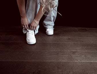 Woman tying white sneakers on dark wood floor