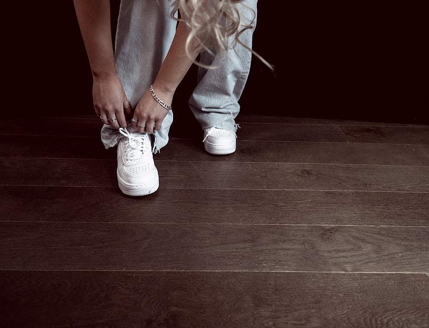 Woman tying white sneakers on dark wood floor