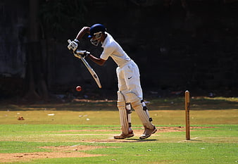 Cricketer playing defensive shot on grass field