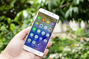 Hand holding white Samsung smartphone with app icons