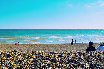Sunny pebble beach with turquoise ocean and people relaxing