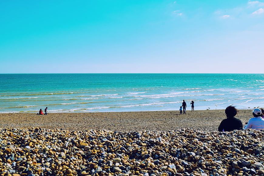Sunny pebble beach with turquoise ocean and people relaxing