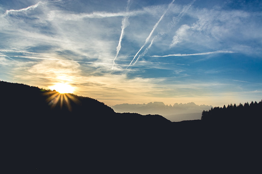 Sunset over mountain silhouette with contrails in blue sky