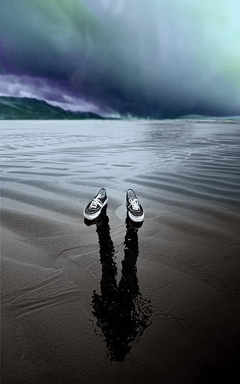Lonely black sneakers on wet sand with dramatic stormy sky