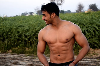Shirtless muscular man smiling outdoors in a green field