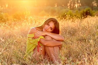 Beautiful Woman Sitting in Golden Meadow at Sunset