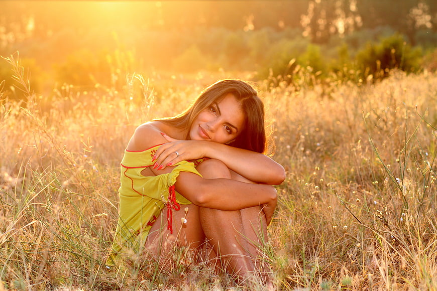 Beautiful Woman Sitting in Golden Meadow at Sunset