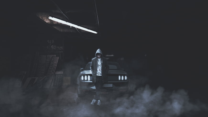 Man in Hoodie Standing in Front of Car in Smoky Garage