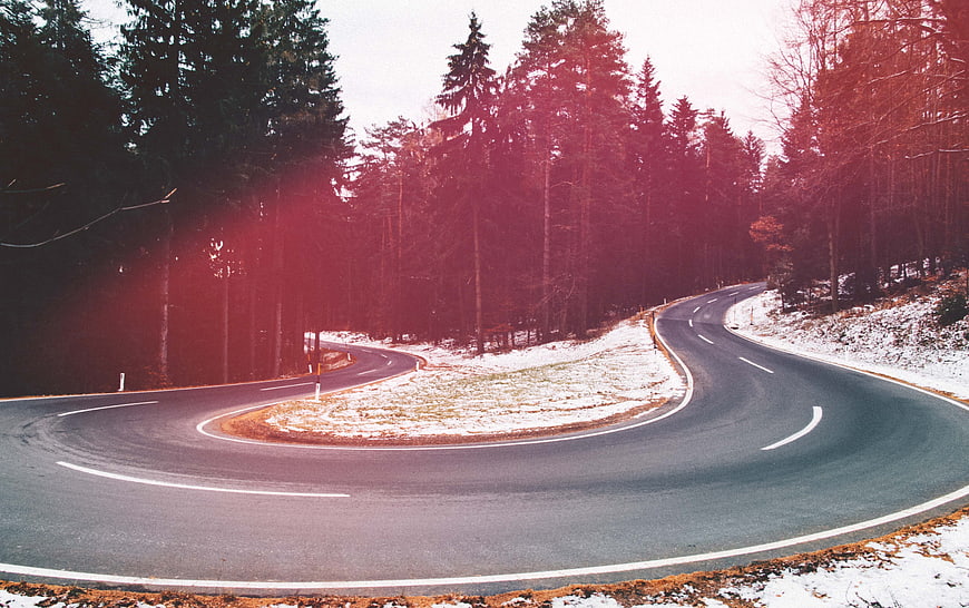 Winding asphalt road through snowy forest with red lens flare
