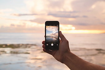 Hand holding smartphone photographing sunset beach landscape