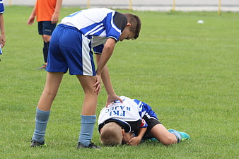 Young footballer injured on grass field with teammate offering help