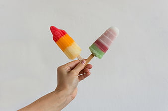 Hand holding two colorful striped popsicles on white background