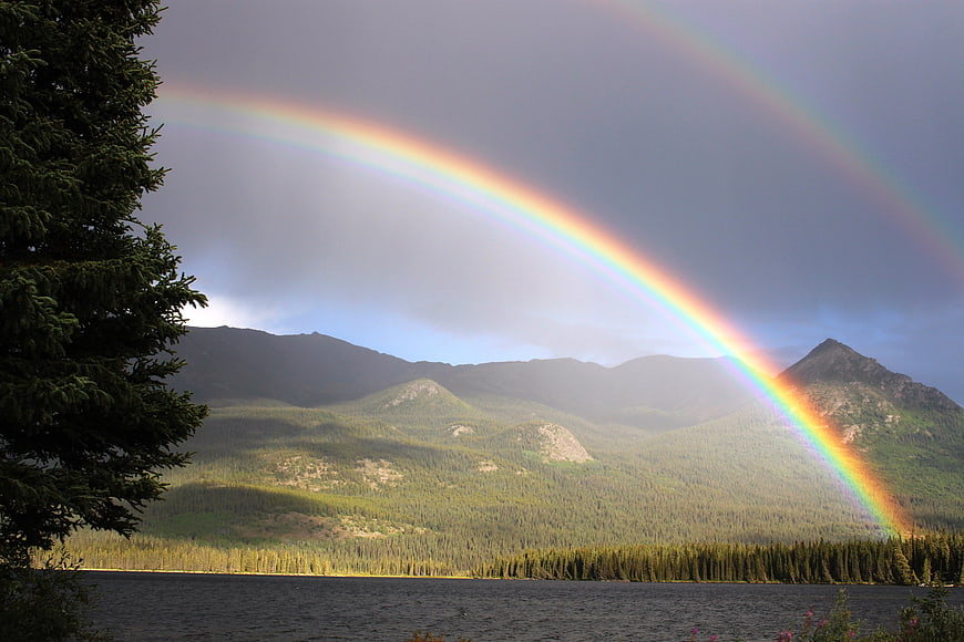 Double rainbow over forested mountains and lake in British Columbia