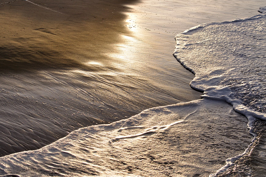 Golden sunlight reflecting on wet sand with ocean waves