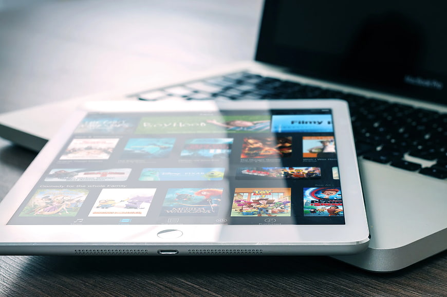 White tablet displaying movie apps on silver laptop