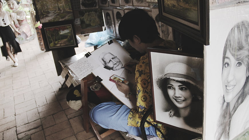 Street artist drawing charcoal portrait on sidewalk