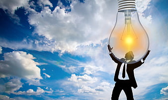 Silhouette of businessman holding giant lightbulb against blue sky