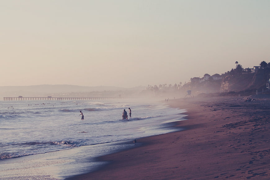 Hazy Sunset Beach Scene with Pier and Surfers