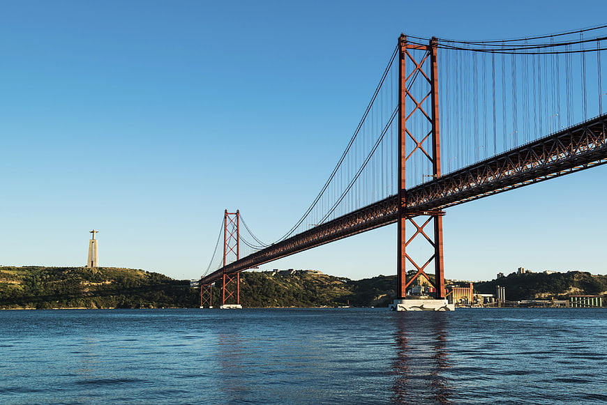 Red suspension bridge over river with Christ statue in background