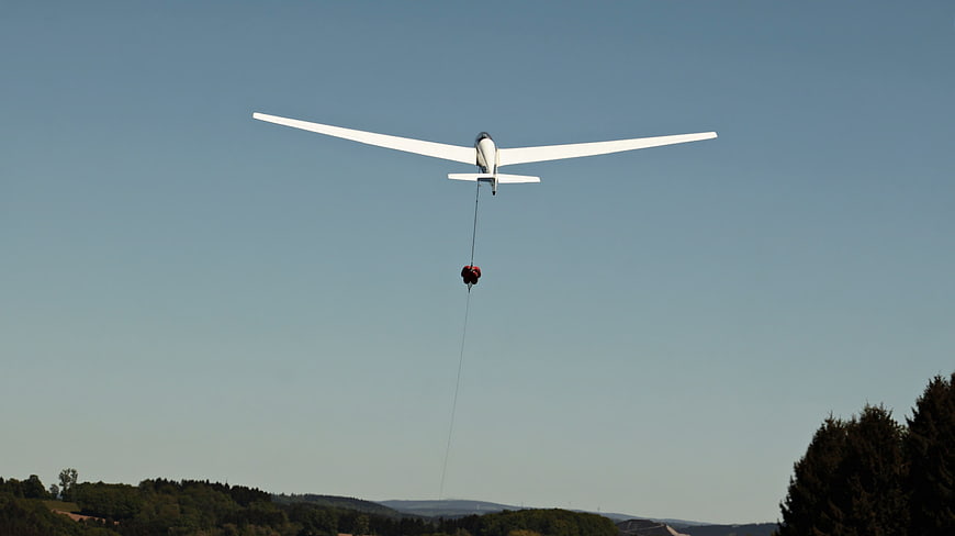 Glider Aircraft Towing Parachute Pilot Across Clear Blue Sky