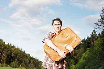 Young man holding vintage leather suitcase in forest landscape