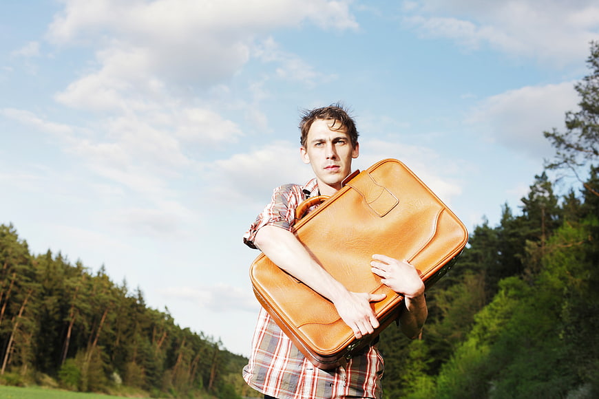 Young man holding vintage leather suitcase in forest landscape