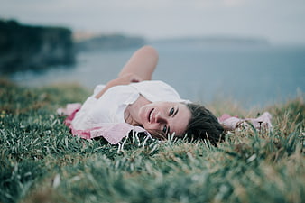 Young woman lying in grass on coastal cliff