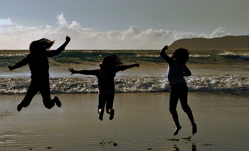 Silhouettes of three children jumping on a beach at sunset