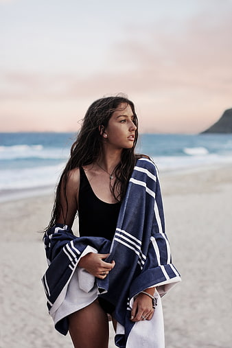 Woman in black swimsuit wrapped in towel on beach at sunset