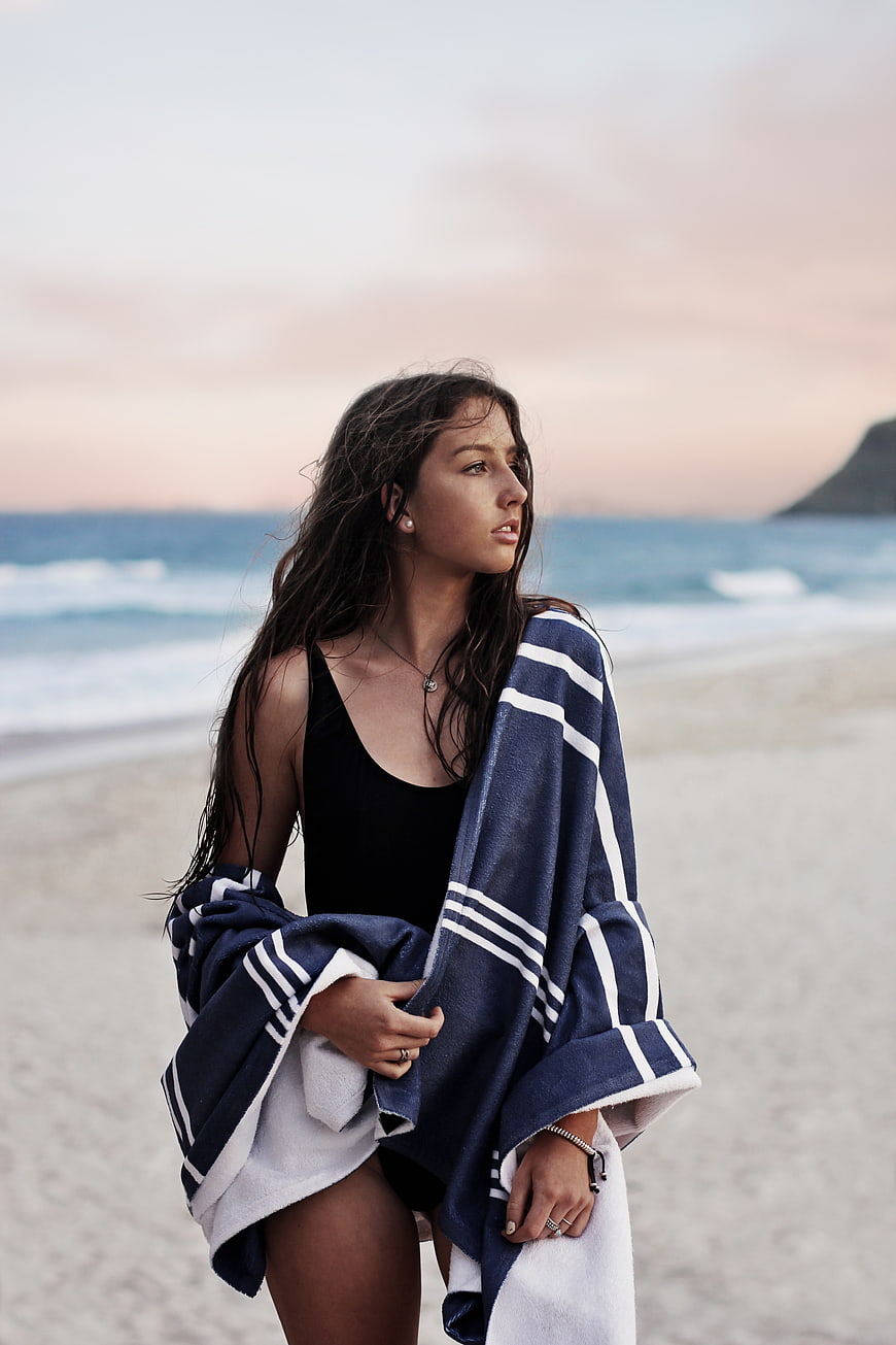 Woman in black swimsuit wrapped in towel on beach at sunset