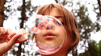 Close-up of child blowing large soap bubble outdoors