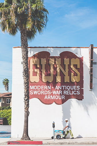 Man walking past vintage Guns mural on white wall