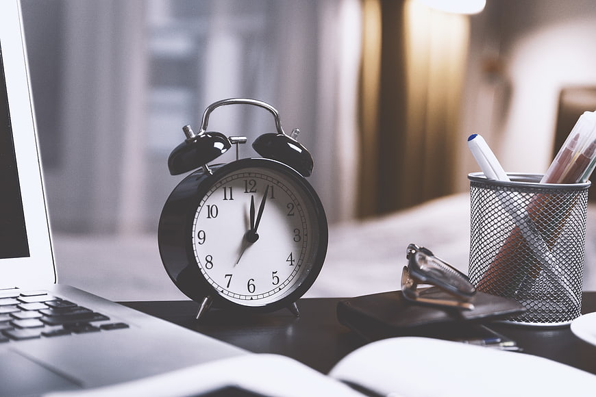 Black alarm clock on desk with laptop and office supplies