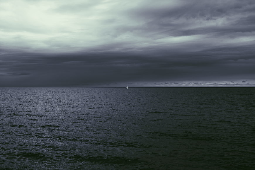 Lone Sailboat on Dark Ocean Under Stormy Clouds