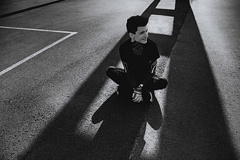 Man Sitting in Shadows on Asphalt