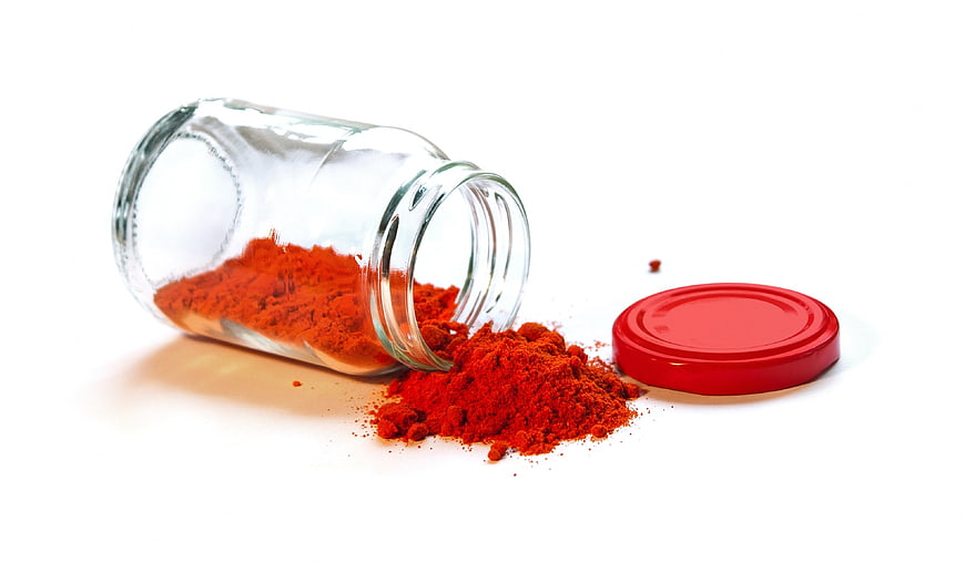 Glass jar with red spice powder on white background