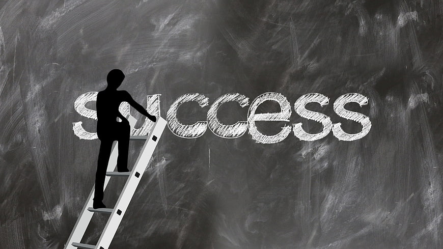 Silhouette of person climbing ladder to reach success word on chalkboard