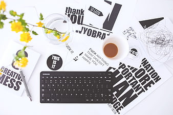 Flat lay of creative workspace with keyboard, coffee, and typography prints