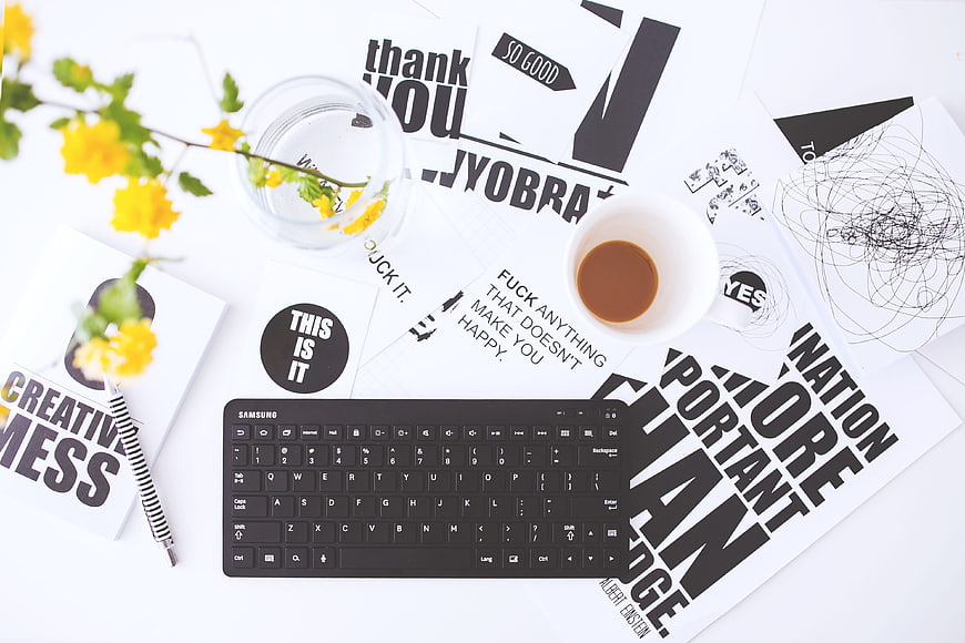Flat lay of creative workspace with keyboard, coffee, and typography prints