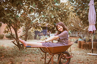 Woman relaxing in rusty wheelbarrow under tree