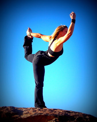 Woman performing yoga pose on rock against blue sky