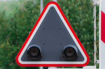 Close-up of a triangular railroad crossing warning sign with two black speakers