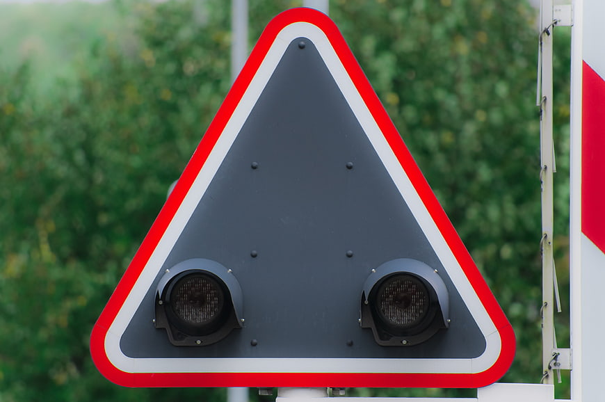 Close-up of a triangular railroad crossing warning sign with two black speakers