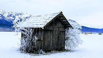 Rustic wooden hut in snowy winter landscape with mountains