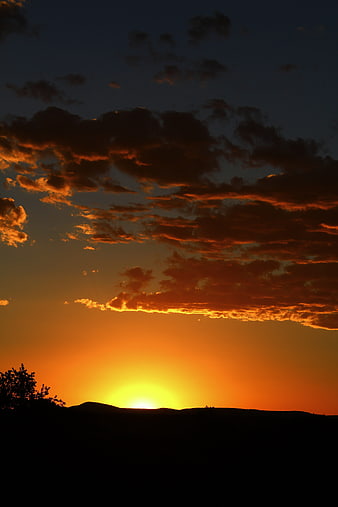 Dramatic sunset with orange clouds over silhouetted hills