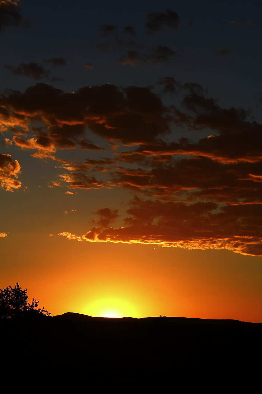 Dramatic sunset with orange clouds over silhouetted hills
