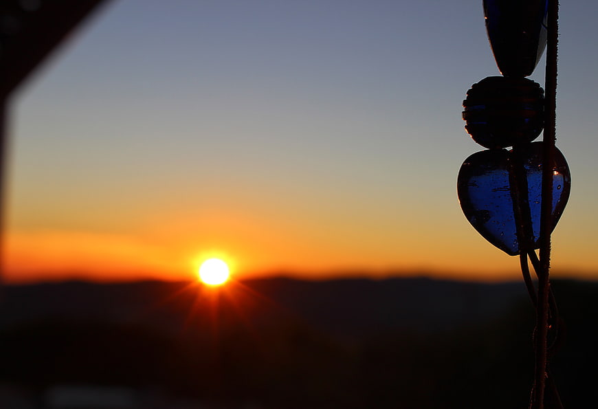Blue glass heart wind chime silhouette against sunset