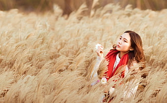 Asian woman in red scarf standing in golden reed field