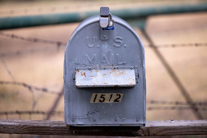 Vintage U.S. Mailbox with Rusty Flag on Wooden Fence